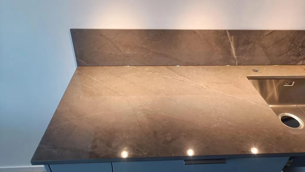 Detalj av polerad Dekton Korso med kranhål, diskho och stänkskydd över grå köksstommar i Göteborg.