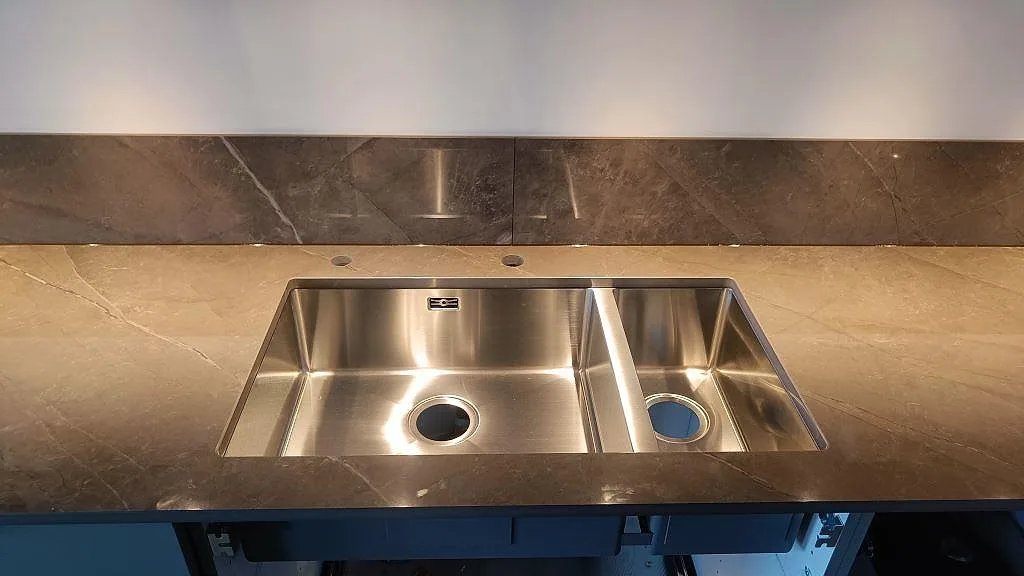 Närbild på dubbel underlimmad rostfri diskho i polerad Dekton Korso med brungrå ådring i Göteborg.