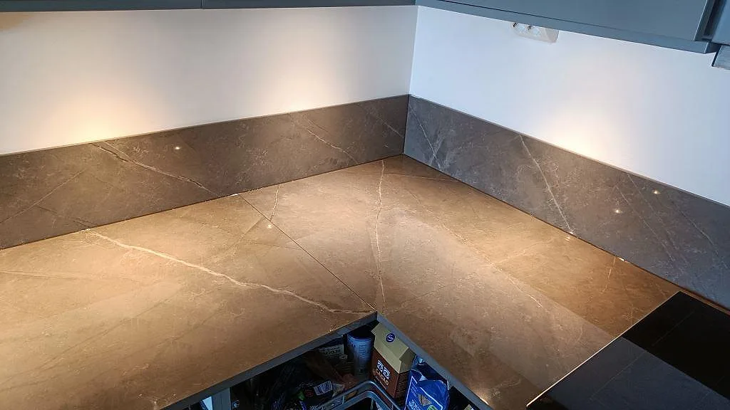 Hörn i U-format kök med polerad Dekton Korso, brungrå ådring och lågt stänkskydd i Göteborg.