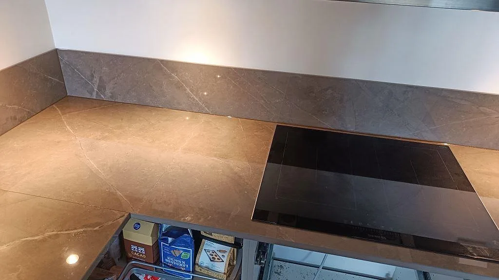 Polerad Dekton Korso runt en svart induktionshäll med matchande stänkskydd i ett kök i Göteborg.