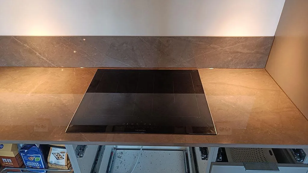 Svart induktionshäll infälld i köksbänkskiva av polerad Dekton Korso med 8 mm stänkskydd i Göteborg.