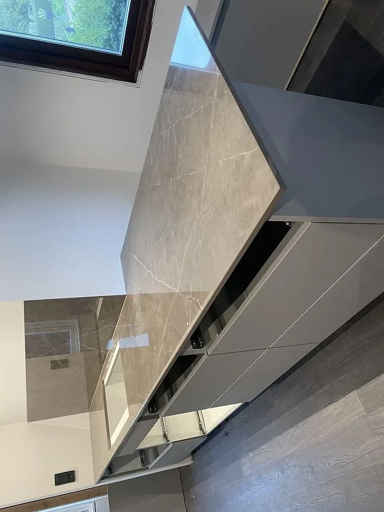 Stor köksö med polerad bänkskiva i Dekton Korso keramik, vita stommar och blankt stänkskydd i ett kök i Häljarp.