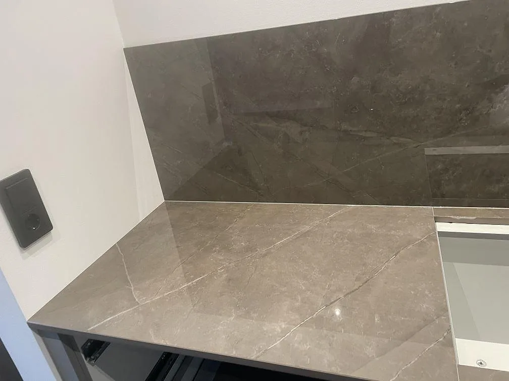 Hörnvy av Dekton Korso bänkskiva och 8 mm stänkskydd i polerad keramik under montering i Häljarp.