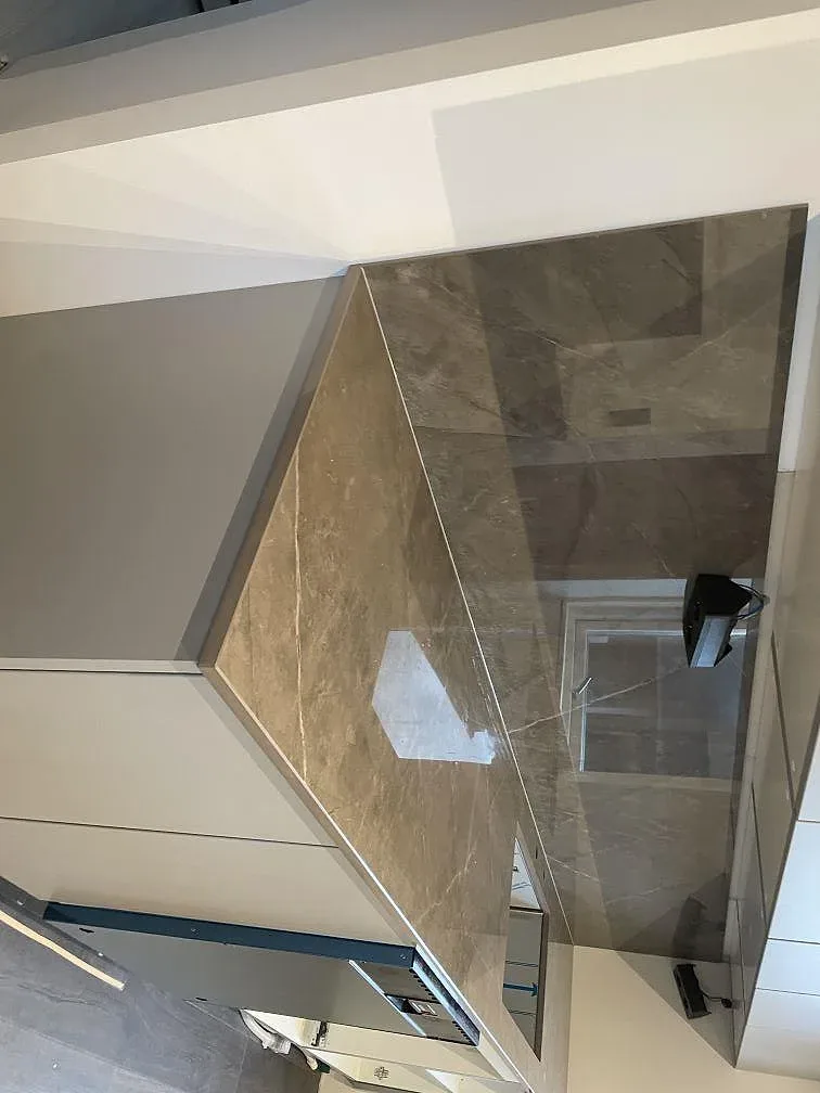 Sidovy av köksö och blankt stänkskydd i polerad Dekton Korso keramik under montering i Häljarp.