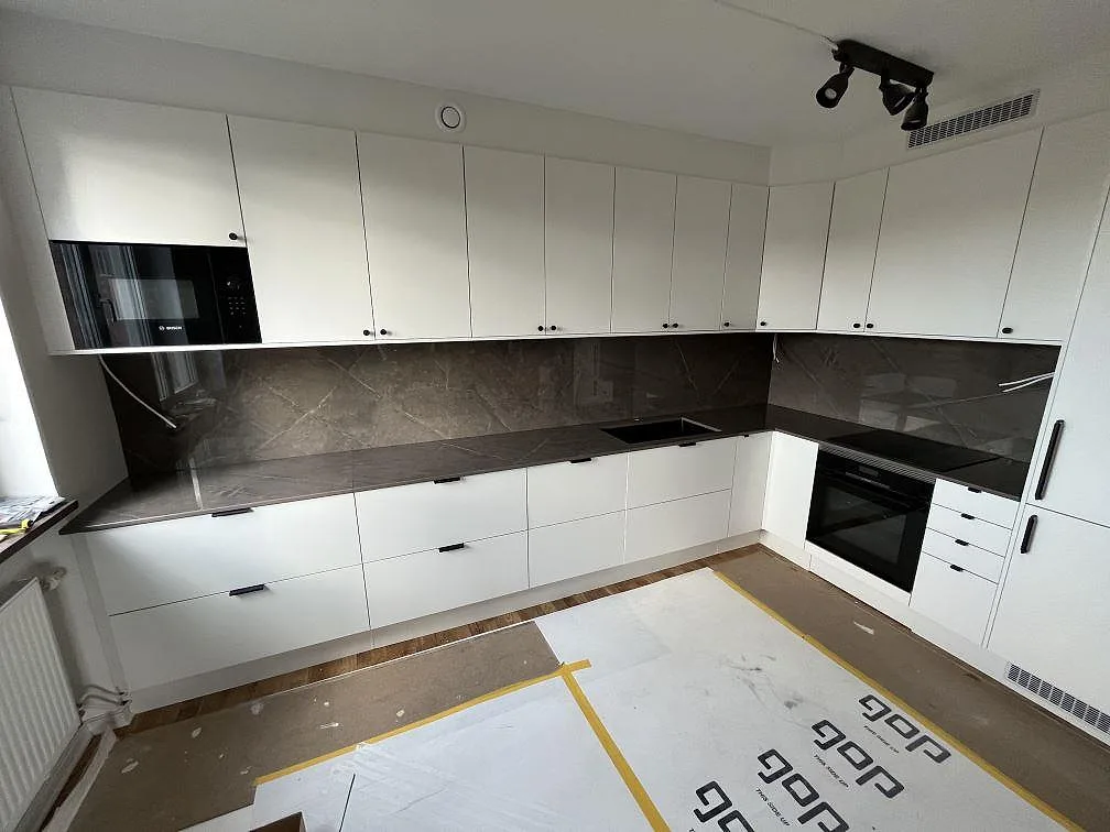 L-format kök i Johanneshov med polerad bänkskiva och stänkskydd i Dekton Korso, mörkgrå keramik och vit köksinredning.
