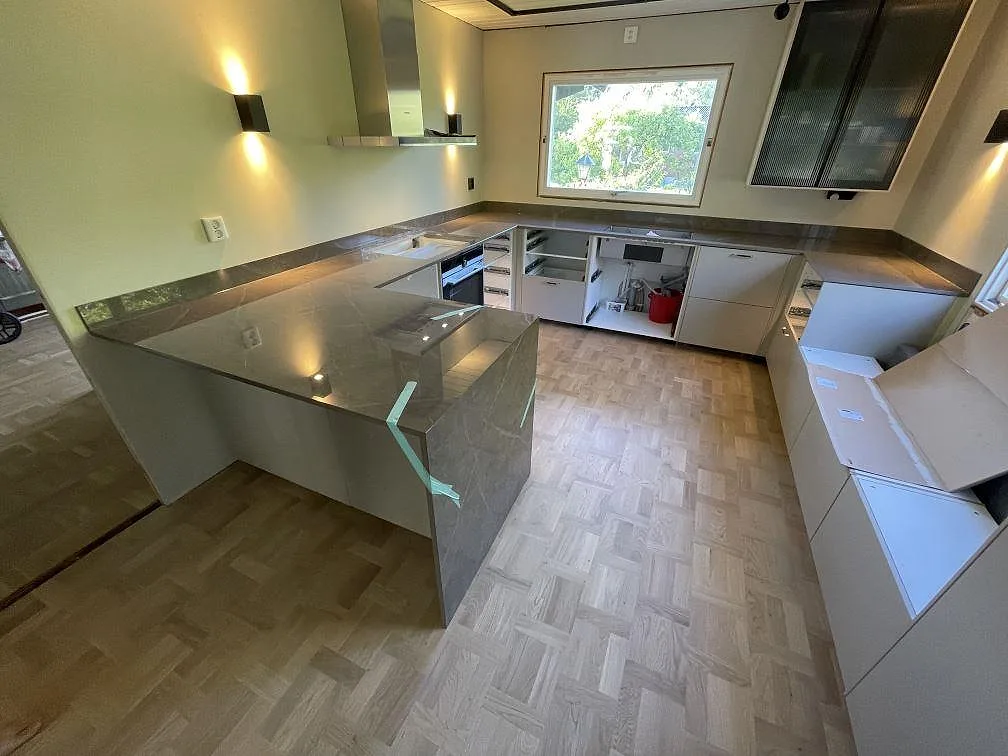 Köksbänkskiva i grå Dekton Korso, polerad keramik, i U-format med halvö och 8 mm stänkkant i Kullavik.