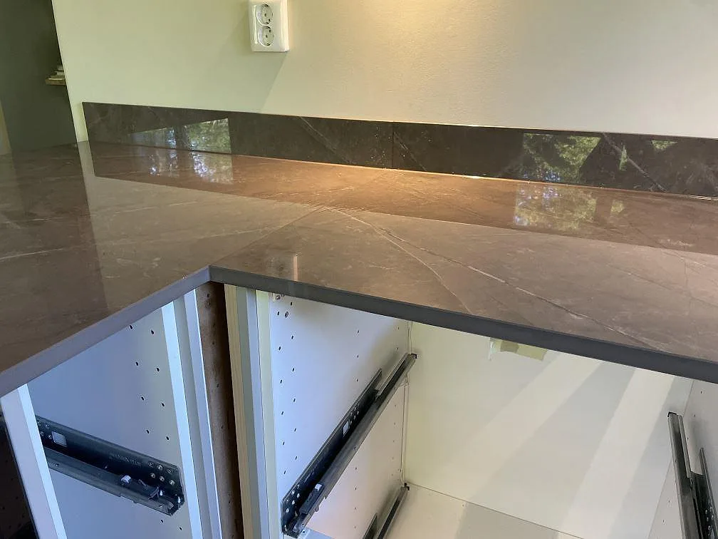 Polerad Dekton Korso som arbetsyta längs vägg med monterad stänkkant och öppna köksstommar i Kullavik.