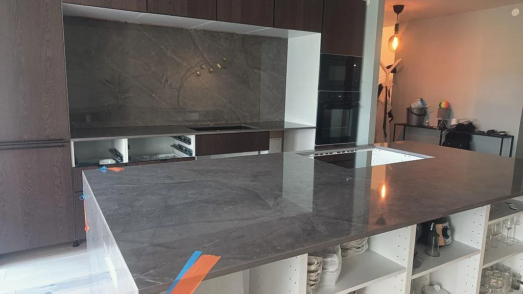 Köksbänkskiva i polerad Dekton Korso med stor köksö och matchande stänkskydd under montering i Staffanstorp.
