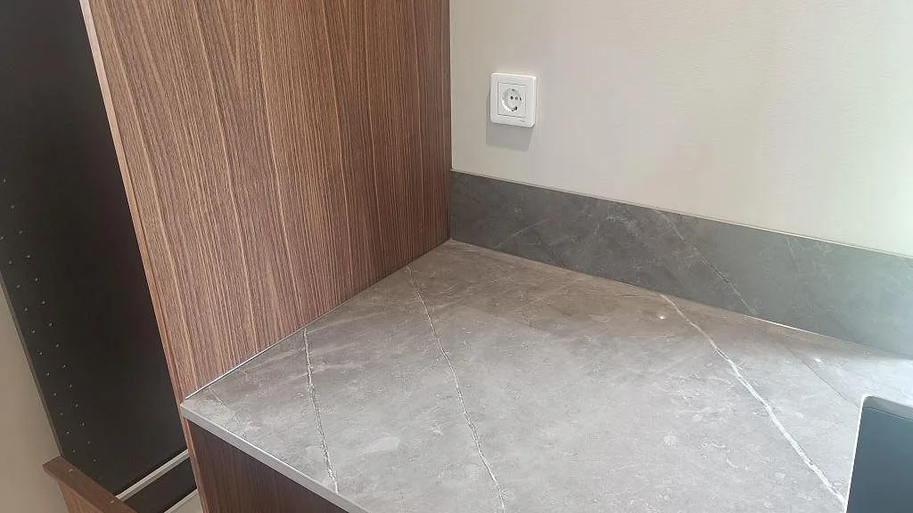 Polerad Dekton Korso som köksbänk med låg stänkkant och grå ådring mot valnötsinredning i Trollhättan.