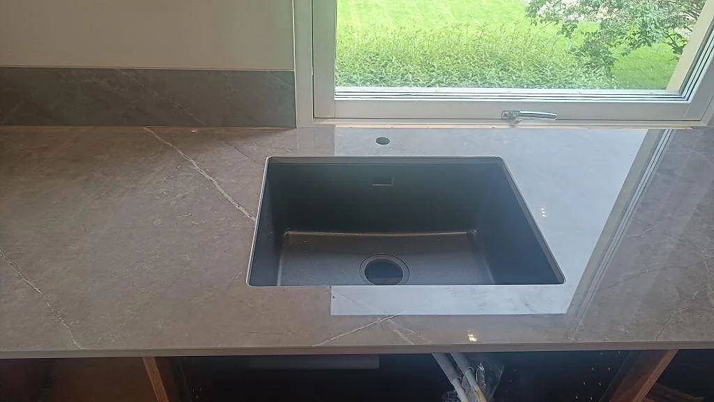 Bänkskiva i polerad Dekton Korso med underlimmad mörk diskho och lågt stänkskydd vid fönster i Trollhättan.