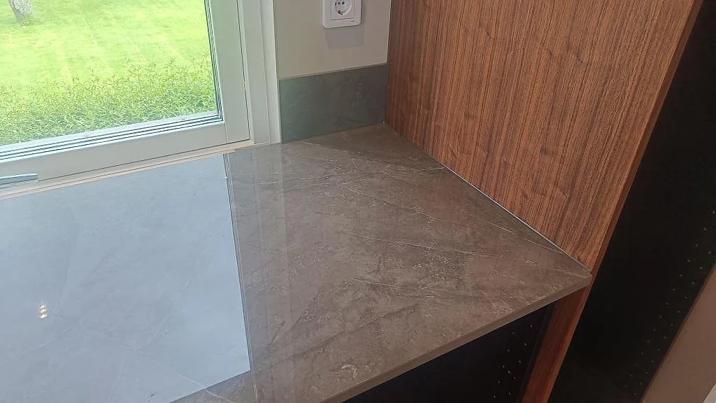 Detalj av polerad bänkskiva i Dekton Korso vid fönster och valnötsinredning i ett kök i Trollhättan.