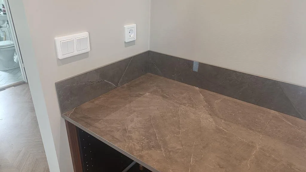 Hörn med polerad Dekton Korso, låg stänkkant och mörk grå keramikyta i kök i Trollhättan.