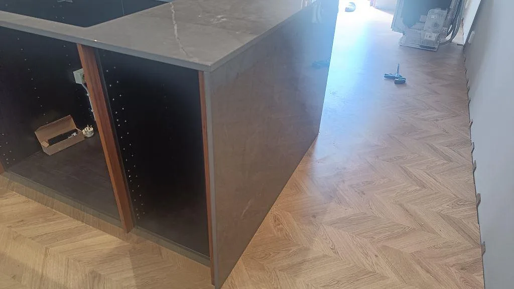 Köksö med vattenfallsida i polerad Dekton Korso och mörk häll i ett kök under montering i Trollhättan.