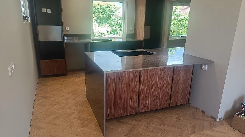 Köksö med polerad bänkskiva i Dekton Korso, mörk keramik och häll i ett kök med valnötsinredning i Trollhättan.