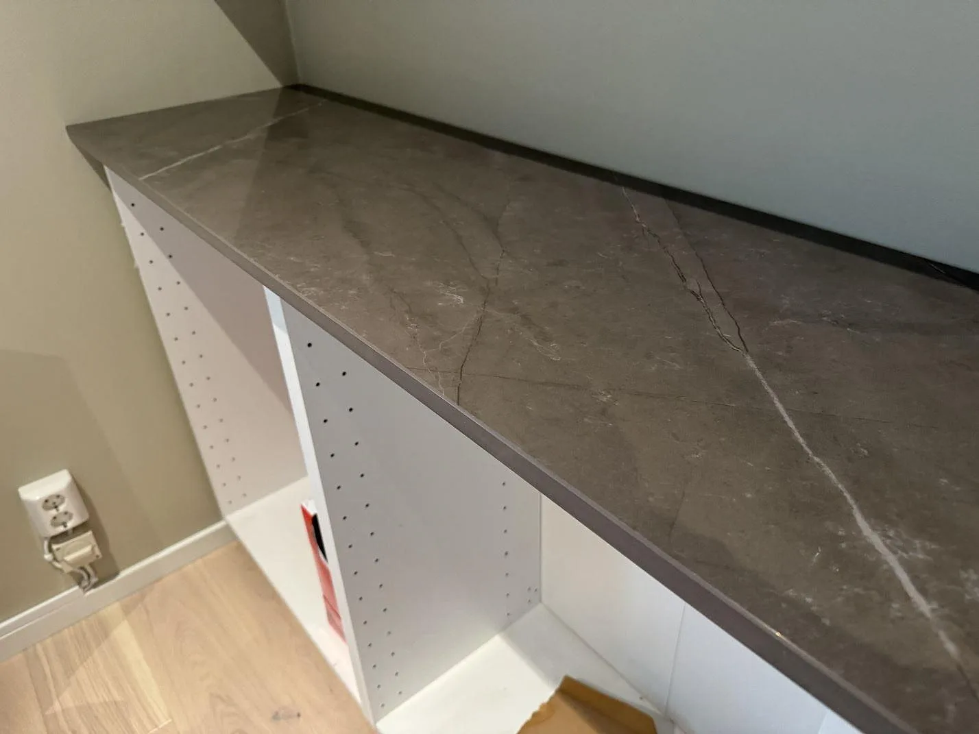 Närbild på sidobänk i polerad Dekton Korso med brun-taupe ådring och öppna hyllstommar i Tygelsjö.