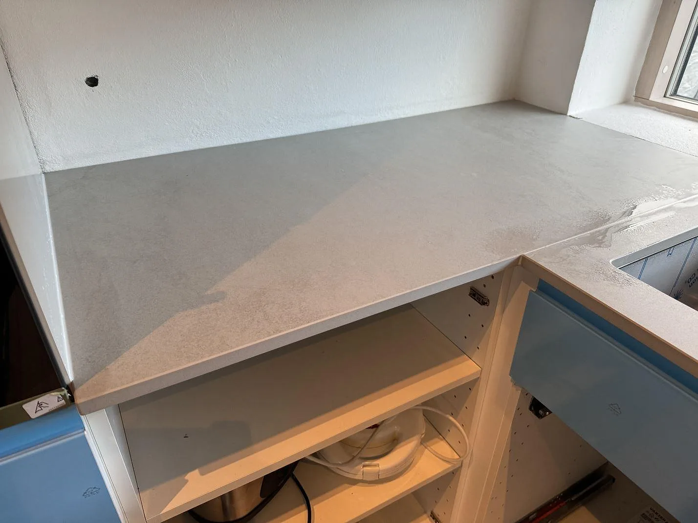 Installerad L-bänkskiva i matt Dekton Kovik över blå köksfronter och öppna stommar i Rydebäck.