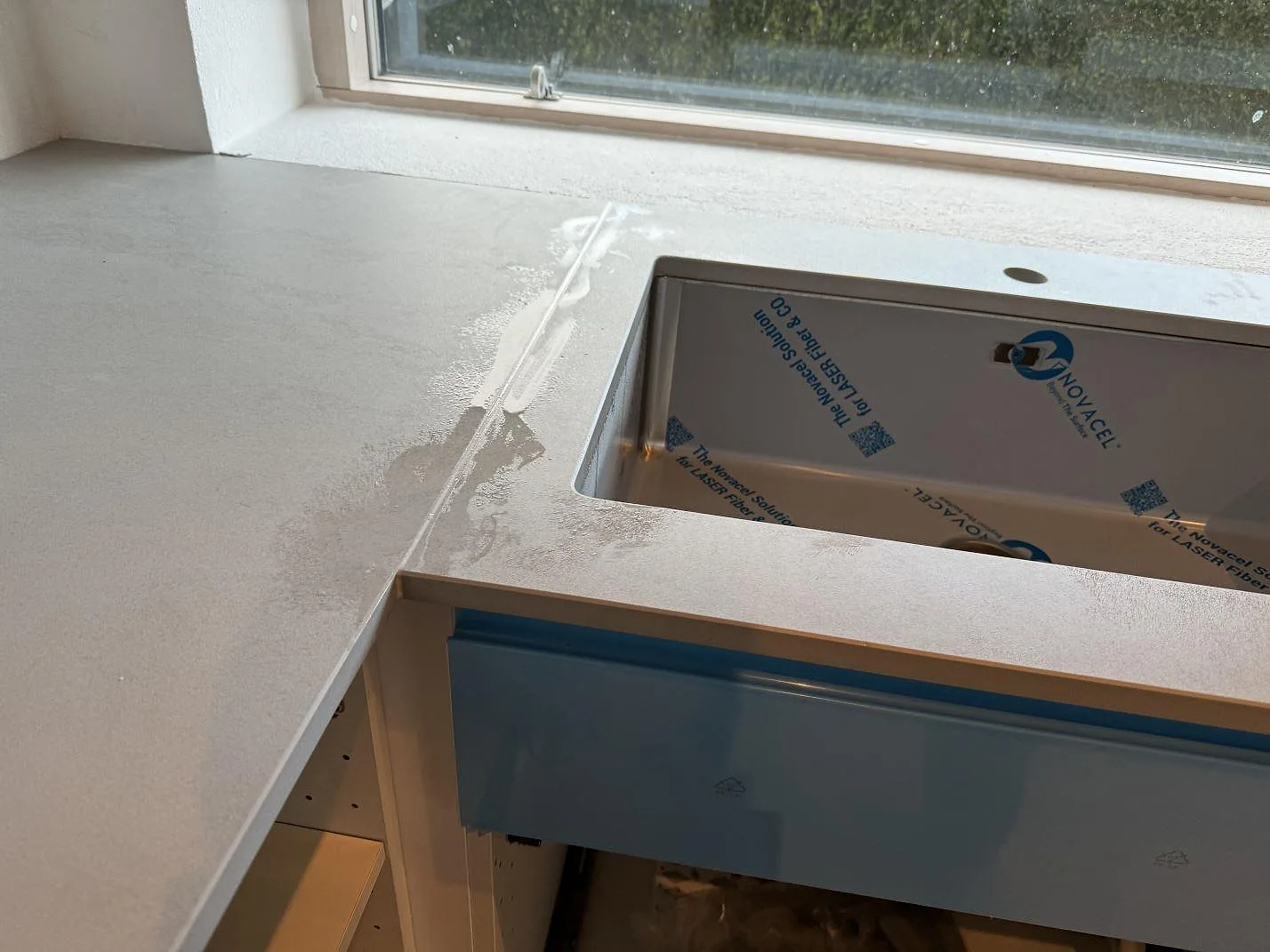 Närbild på underlimmad rostfri diskho i en matt Dekton Kovik-bänkskiva vid fönster i Rydebäck.