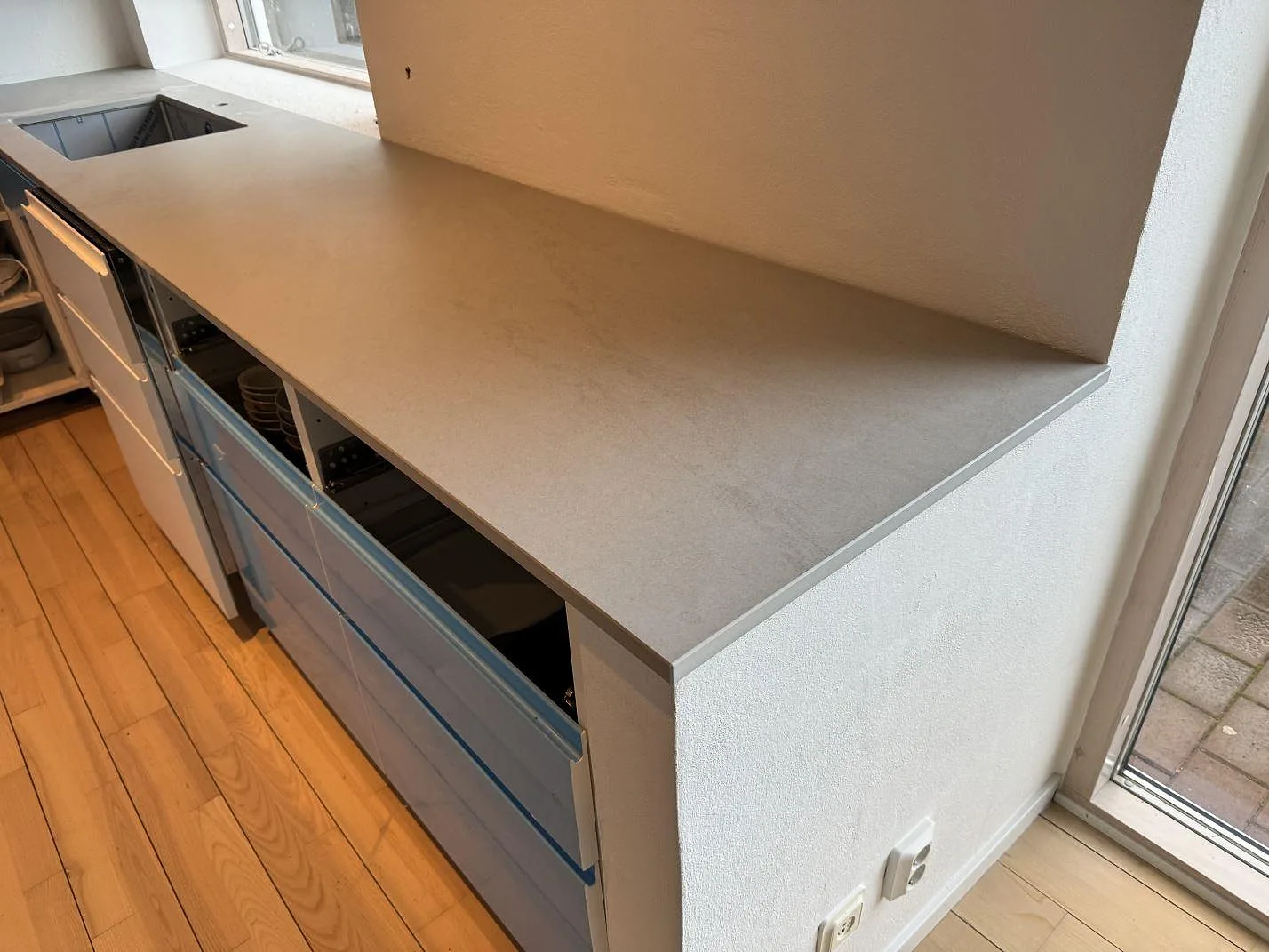 L-formad köksbänkskiva i matt Dekton Kovik med blå frontytor och synlig diskho i köket i Rydebäck.