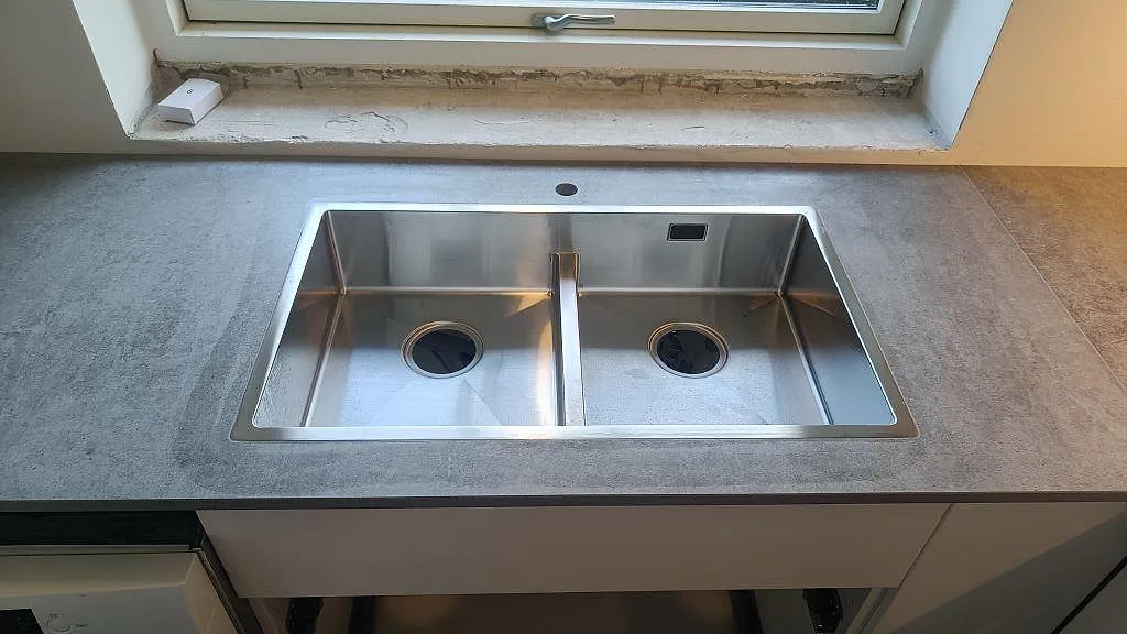 Köksbänkskiva i matt Dekton Kreta, keramik, med rostfri dubbelho under fönster i ett kök i Albertslund.