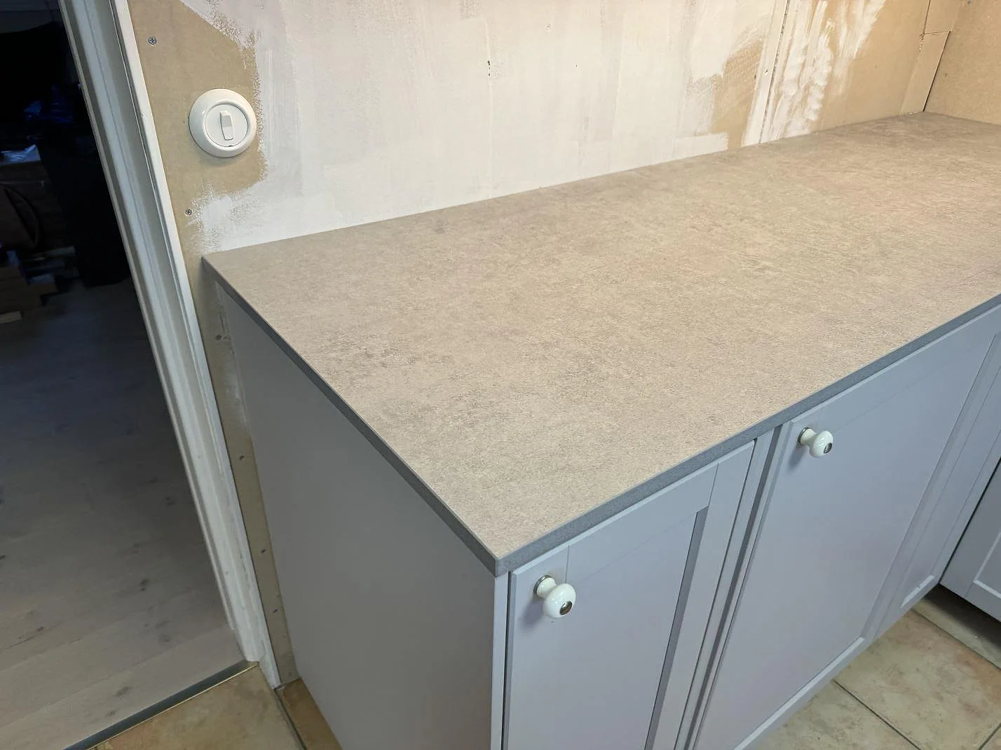 Detalj av matt Dekton Kreta bänkskiva över creamfärgade köksstommar och rå vägg under montering i Karlskrona.