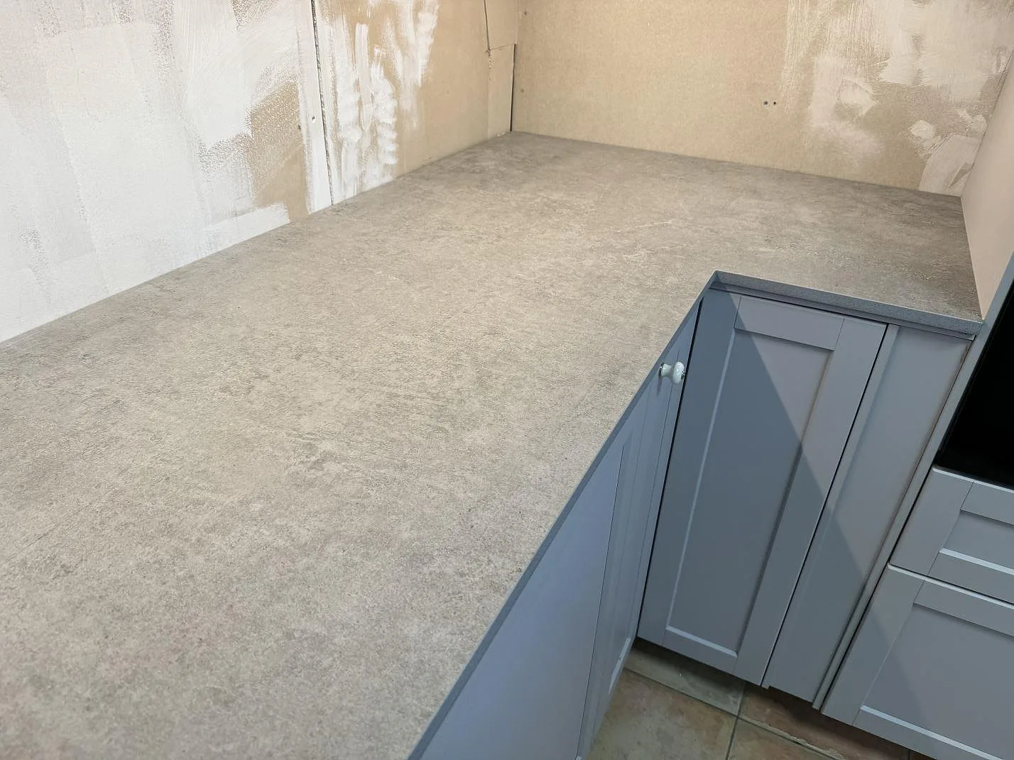 Lång arbetsyta i matt Dekton Kreta med grå betongstruktur över creamfärgade köksluckor i Karlskrona.