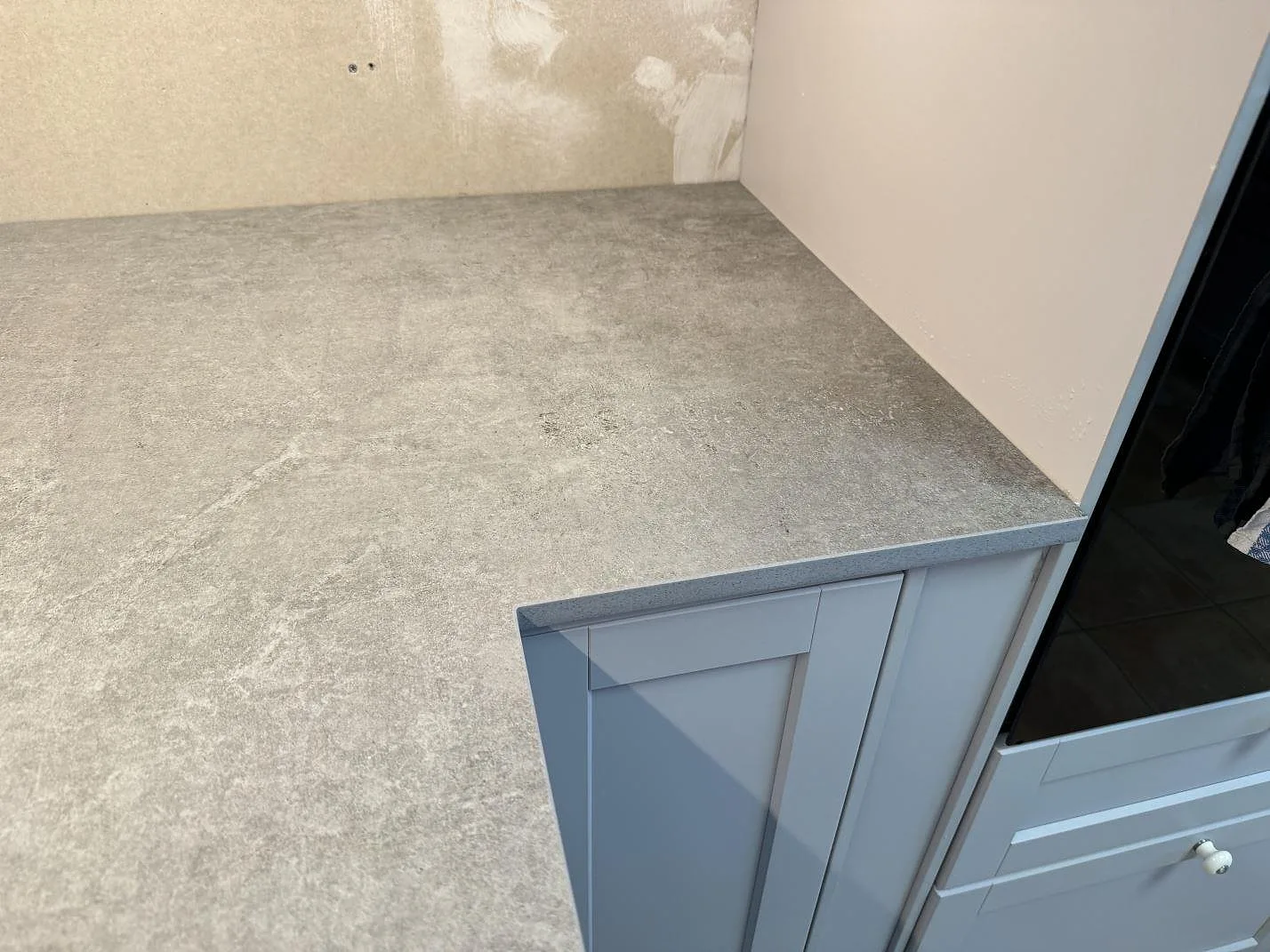 Matt Dekton Kreta köksbänkskiva i hörnläge med grå betongton och synlig framkant under montering i Karlskrona.