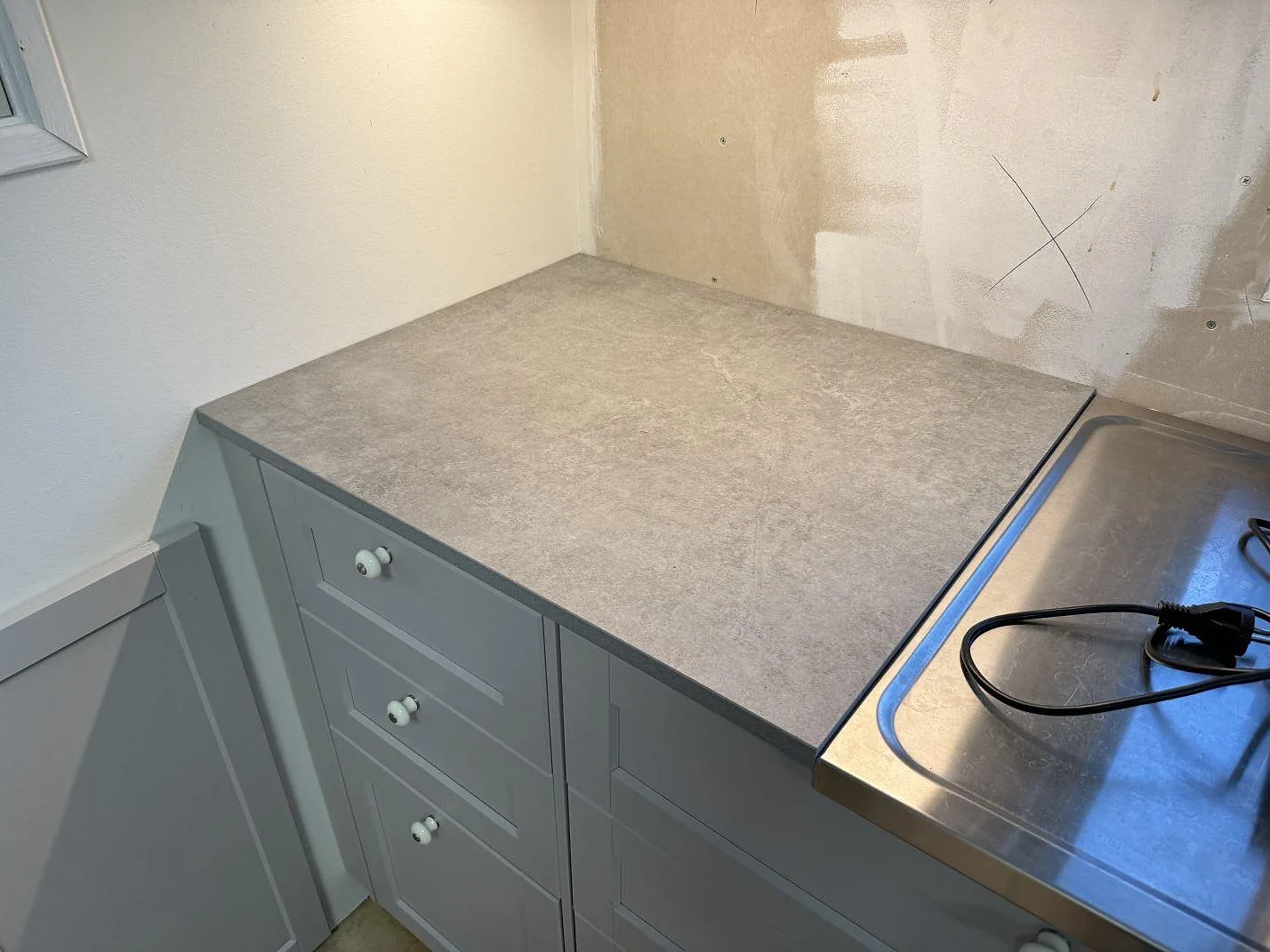 Matt grå köksbänkskiva i Dekton Kreta, 20 mm keramik, monterad över creamfärgade stommar i Karlskrona.
