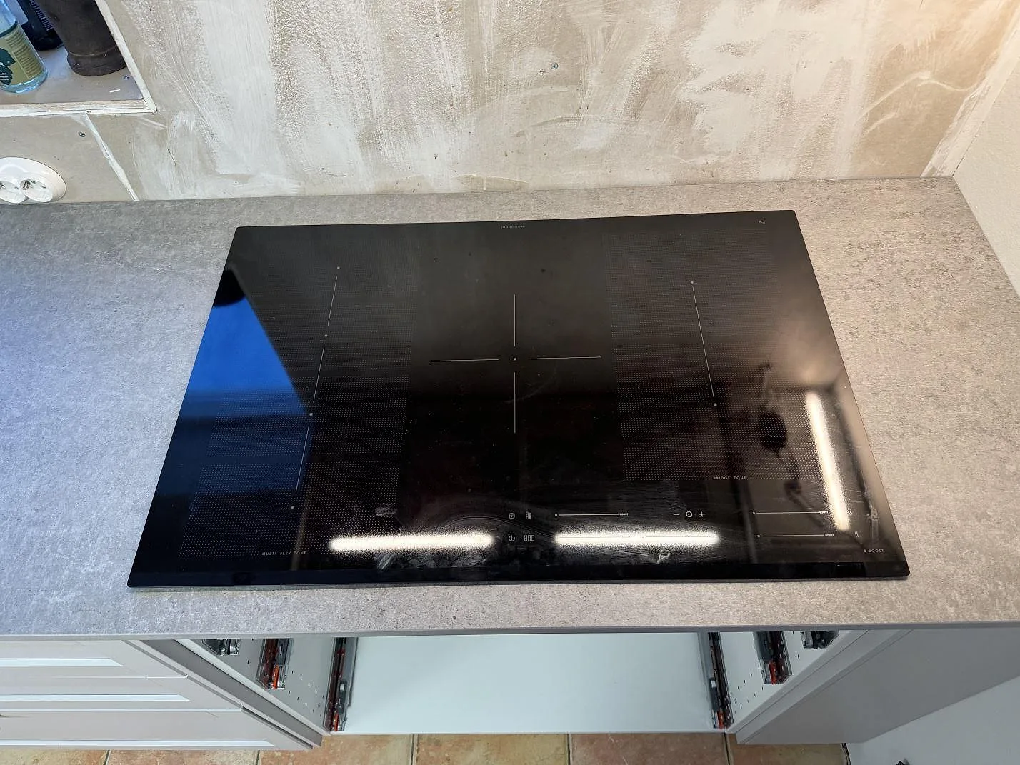 Närbild på svart häll och matt Dekton Kreta bänkskiva, 20 mm keramik, vid rå vägg under köksmontering i Karlskrona.
