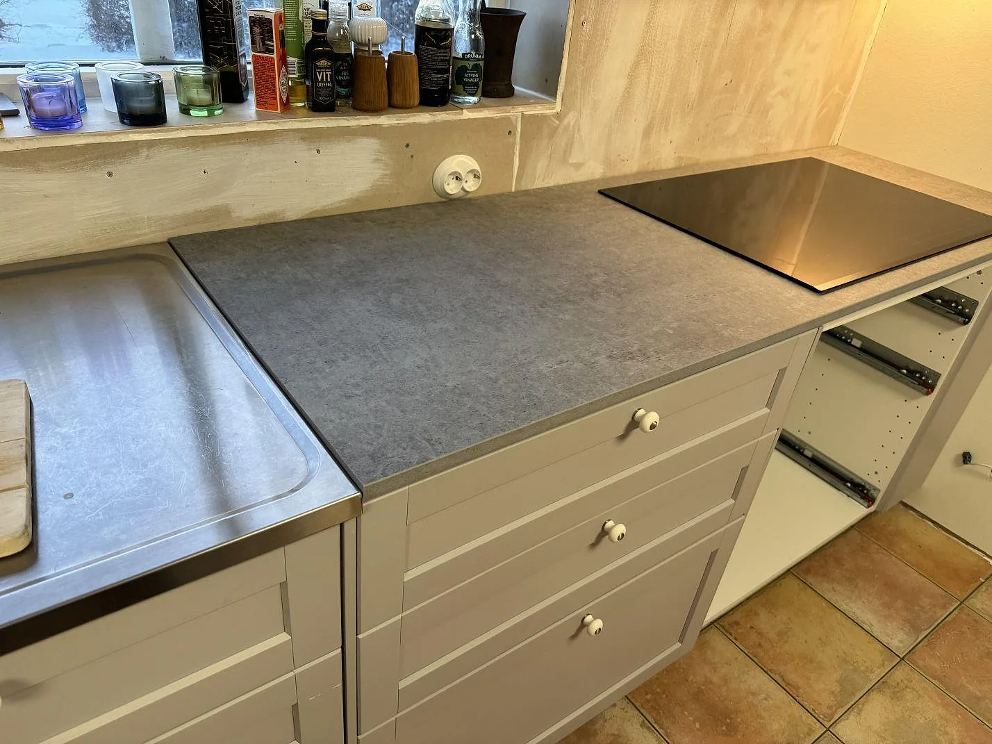 L-formad köksbänkskiva i matt Dekton Kreta, 20 mm keramik, med svart induktionshäll i ett kök under montering i Karlskrona.