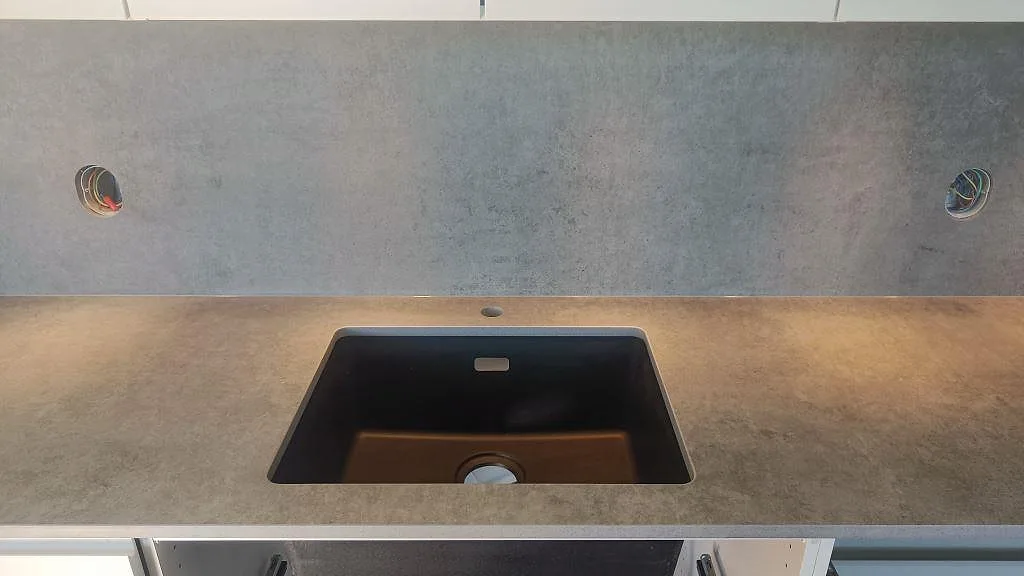 Närbild på svart underlimmad diskho i matt Dekton Kreta med grått stänkskydd och vita skåp i Malmö.