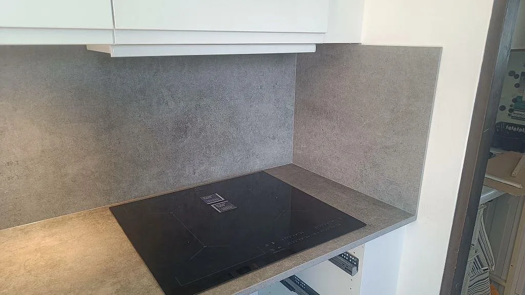 Svart häll infälld i matt Dekton Kreta med grå stänkskyddsskiva och vita överskåp i Malmö.