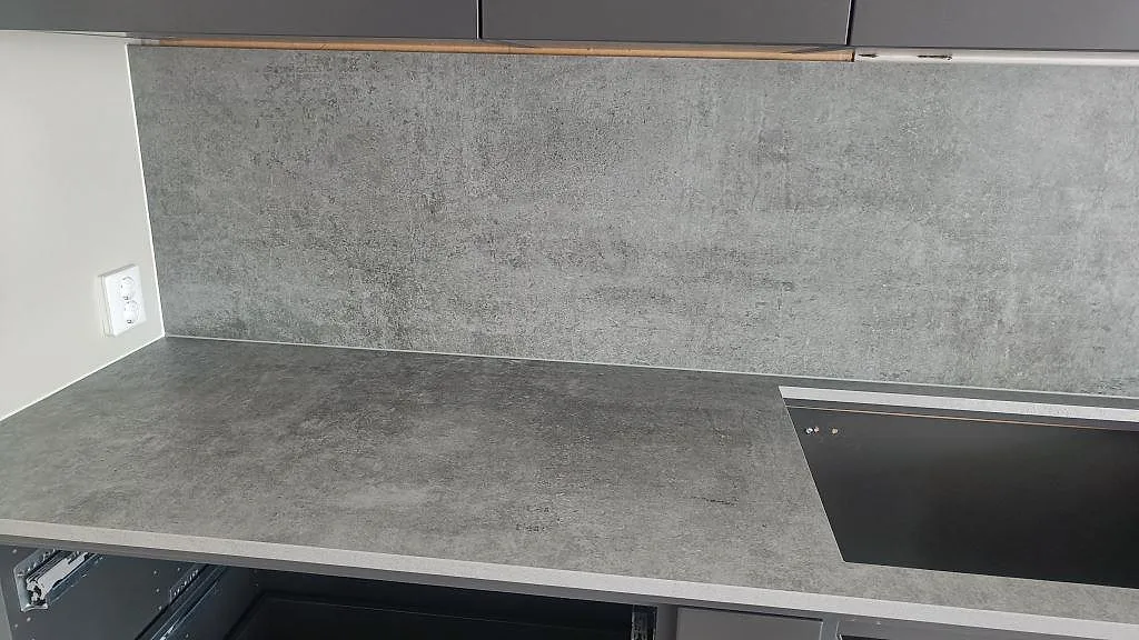 Matt grå Dekton Kreta bänkskiva med stänkskydd i samma sten och infälld induktionshäll längs en köksvägg i Mullsjö.