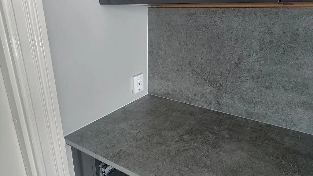 Hörnparti av grå Dekton Kreta köksbänkskiva med uppvikt stänkskydd och betonglik yta i ett kök i Mullsjö.