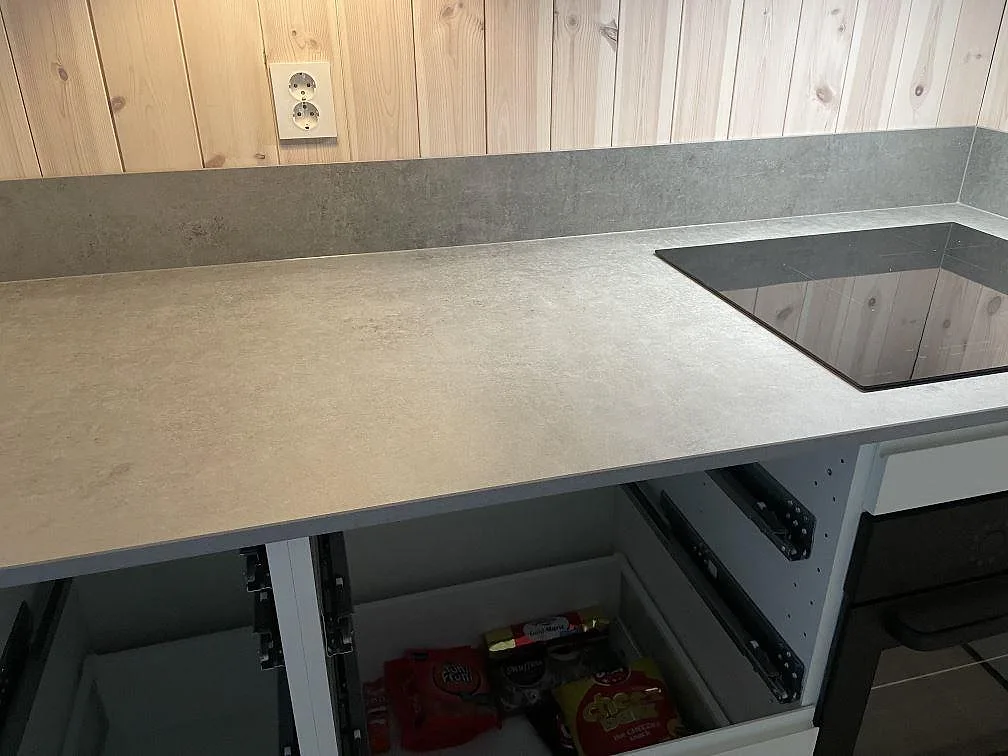 Matt köksbänkskiva i Dekton Kreta keramik med svart induktionshäll, träpanel och öppna köksstommar i Sösdala.