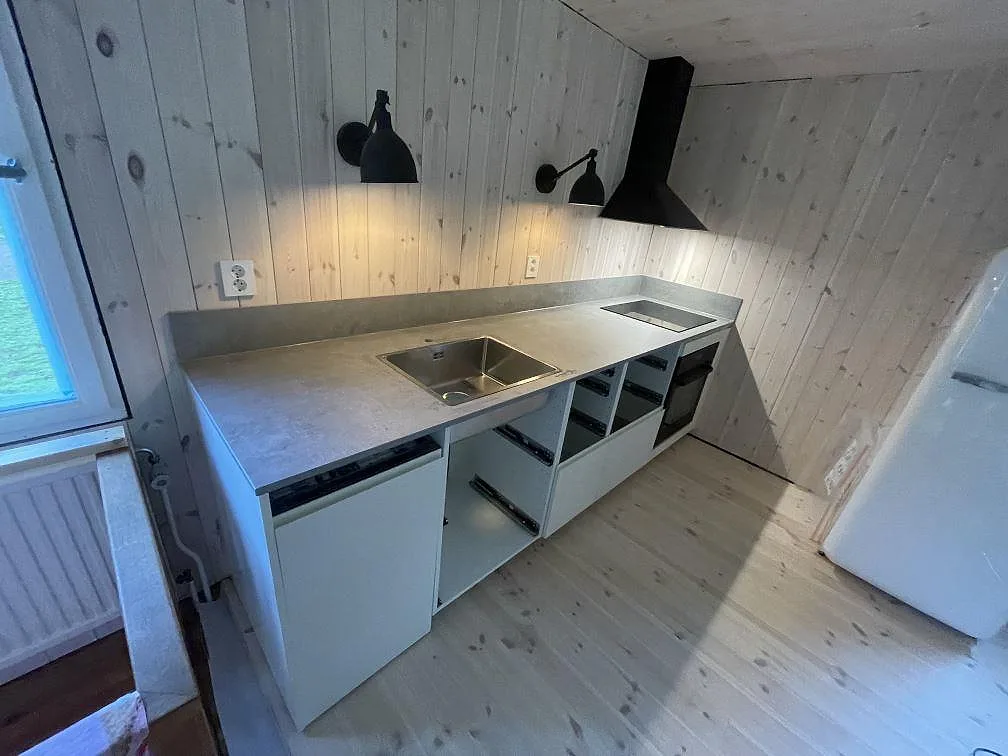 L-formad köksbänkskiva i matt Dekton Kreta keramik med rostfri diskho, svart induktionshäll och stänkskydd i ett kök i Sösdala.