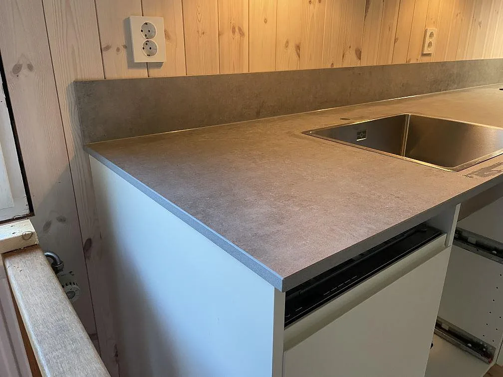 Köksbänkskiva i matt Dekton Kreta keramik med underlimmad rostfri diskho och uppvikt stänkskydd vid fönster i Sösdala.
