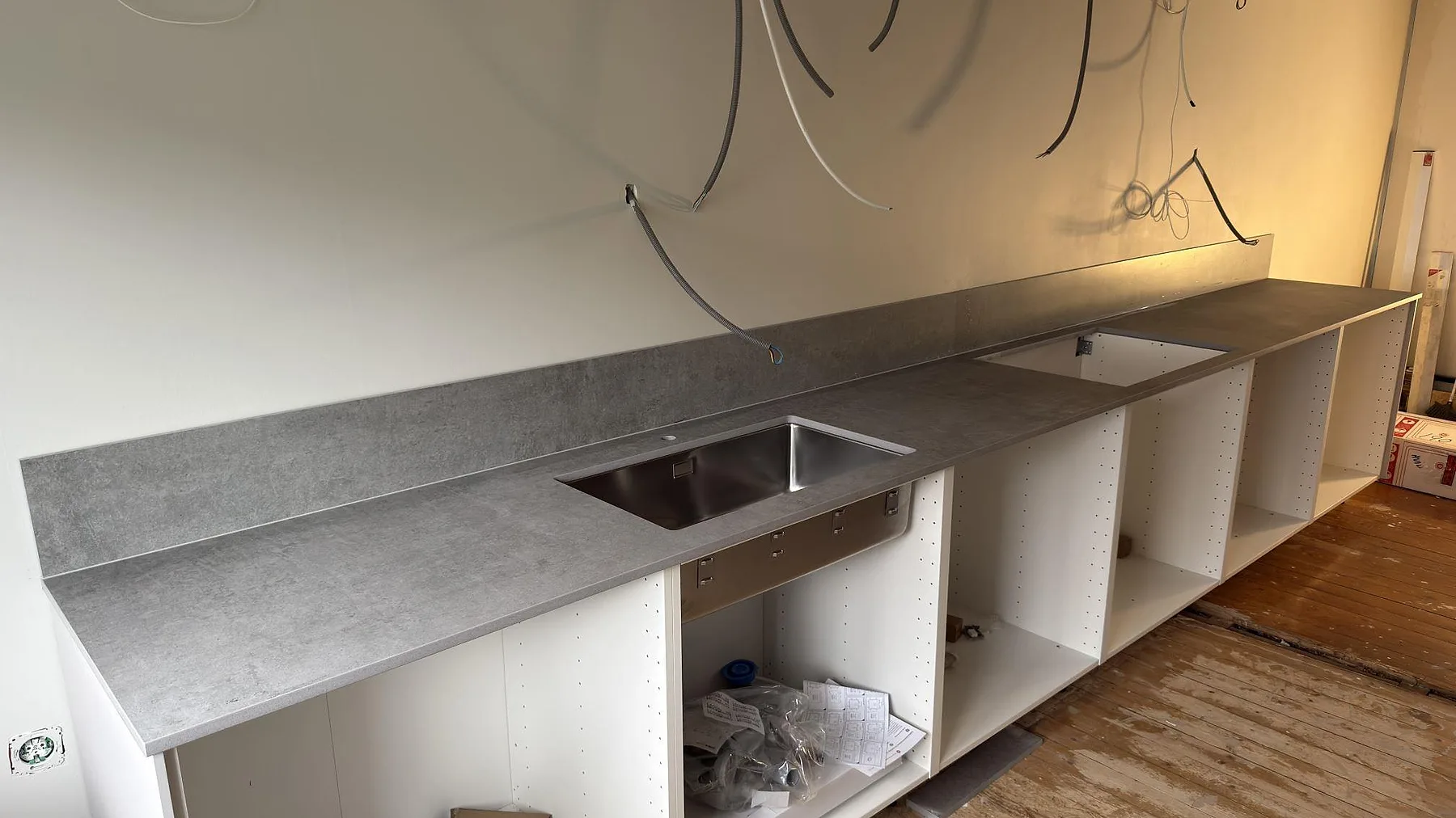 Lång köksbänkskiva i matt Dekton Kreta keramik med underlimmad rostfri diskho, monterad på vita stommar i ett kök i Stockholm.