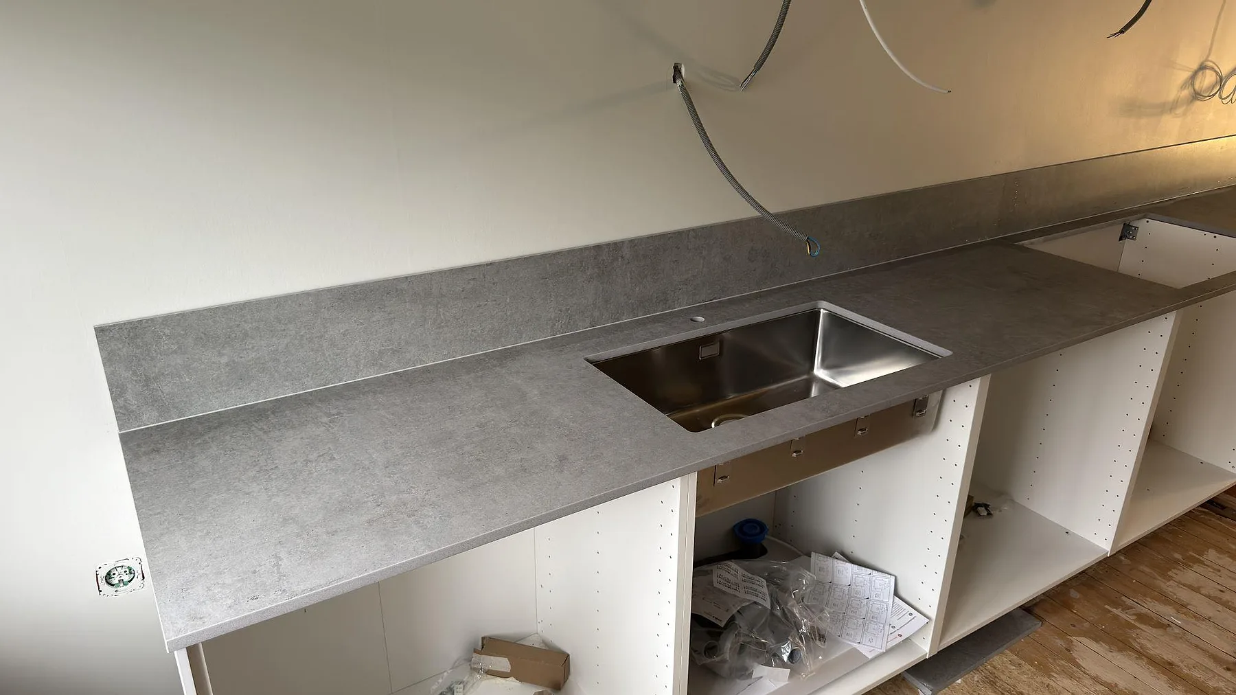 Detalj av matt grå Dekton Kreta köksbänkskiva med underlimmad rostfri diskho i ett kök under montering i Stockholm.
