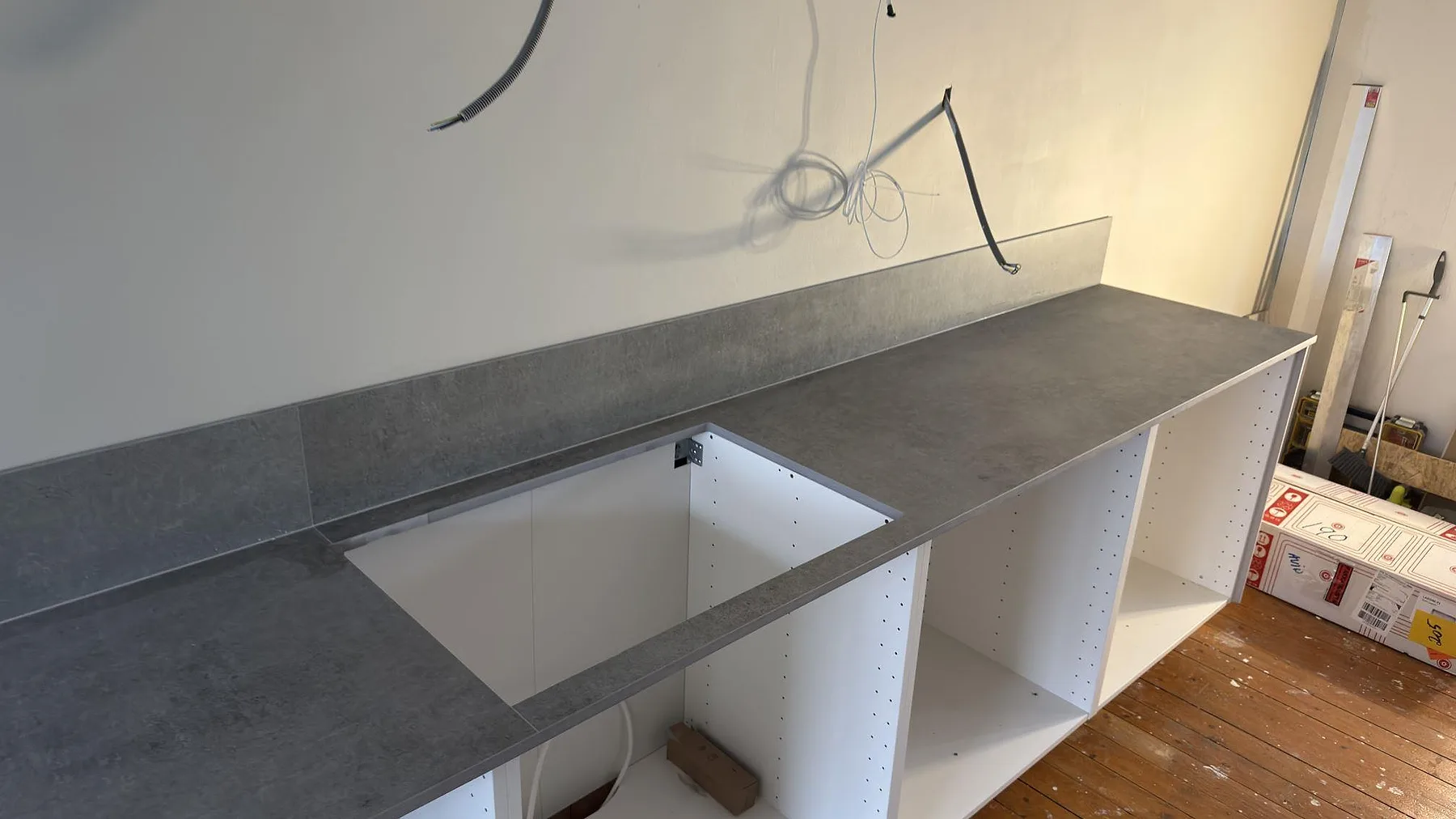 Köksbänkskiva i grå Dekton Kreta keramik med uppvikt stänkkant och förberedd urtagning, sett från motsatt sida i ett kök i Stockholm.