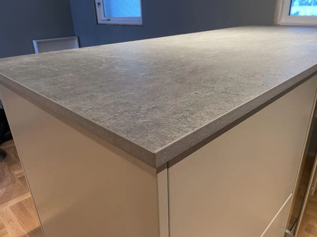Närbild på kant och yta i matt Dekton Kreta keramik på en kökshalvö med grå betongstruktur i TÄBY.