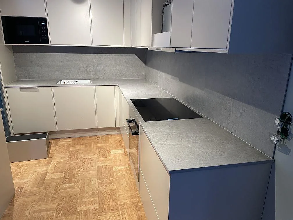 Matt köksbänkskiva i grå Dekton Kreta keramik med svart induktionshäll och matchande stänkskydd i ett U-format kök i TÄBY.