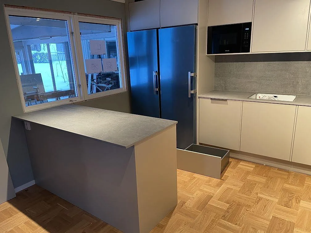 Köksbänkskiva i matt Dekton Kreta keramik med halvö, grå skåpinredning och stänkskydd vid köksväggen i TÄBY.