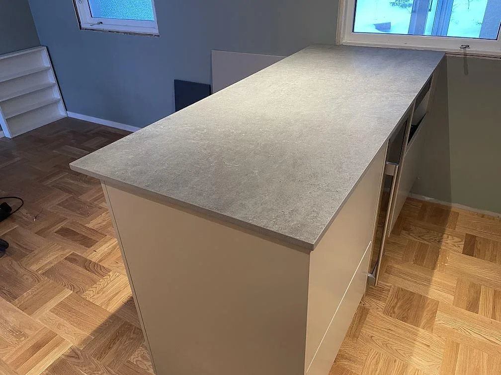 Halvö med 20 mm matt Dekton Kreta köksbänkskiva i grå betonglook, monterad i ett kök med fiskbensparkett i TÄBY.