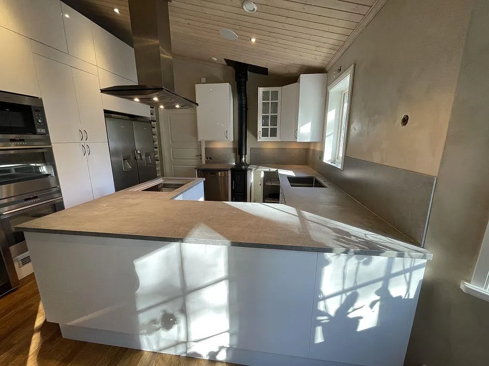 Matt köksbänkskiva i Dekton Kreta sedd från den framskjutna bänkdelen, med grå stänkskyddsskivor och vita köksstommar i Vendelsö.