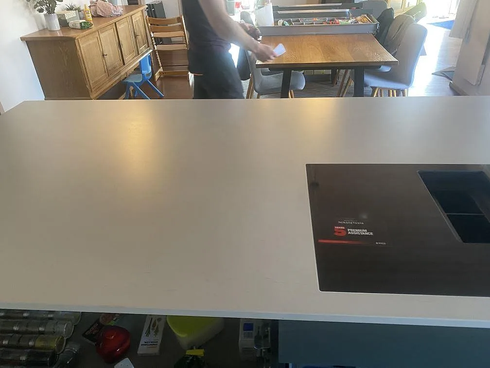Ljusgrå köksö i matt Dekton Laguna Velvet med svart häll och öppen matplats i bakgrunden i Hvidovre.