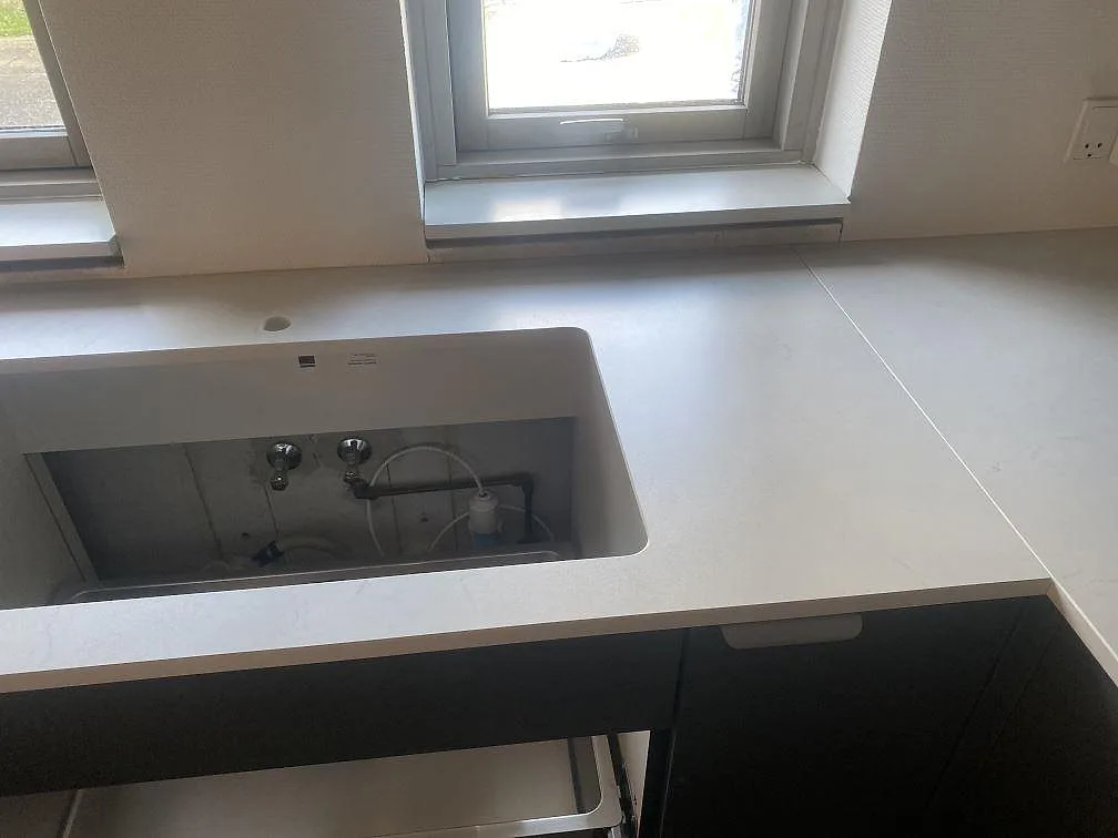 Detalj av ljusgrå Dekton Laguna Velvet bänkskiva med utskärning vid diskzonen och fönster i Hvidovre.