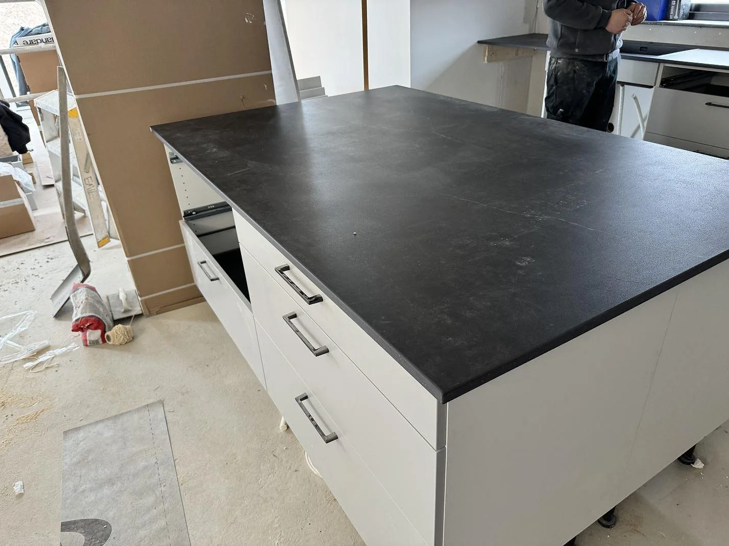 Köksö med matt Dekton Laos, mörk keramikbänkskiva, på vita köksskåp under montering i Halmstad.