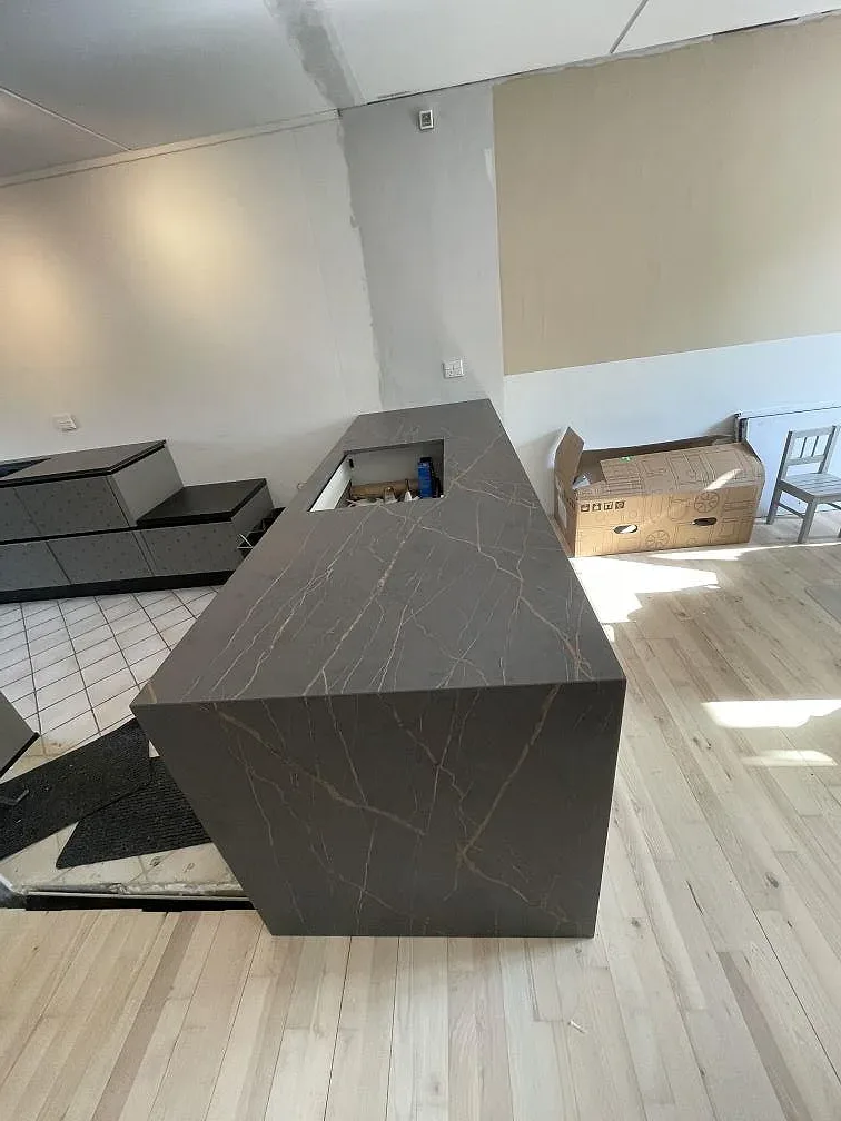 Halvö i Dekton Laurent med vattenfallskant och guldådrigt mönster, sett från sidan i ett kök under montering i Allerød.