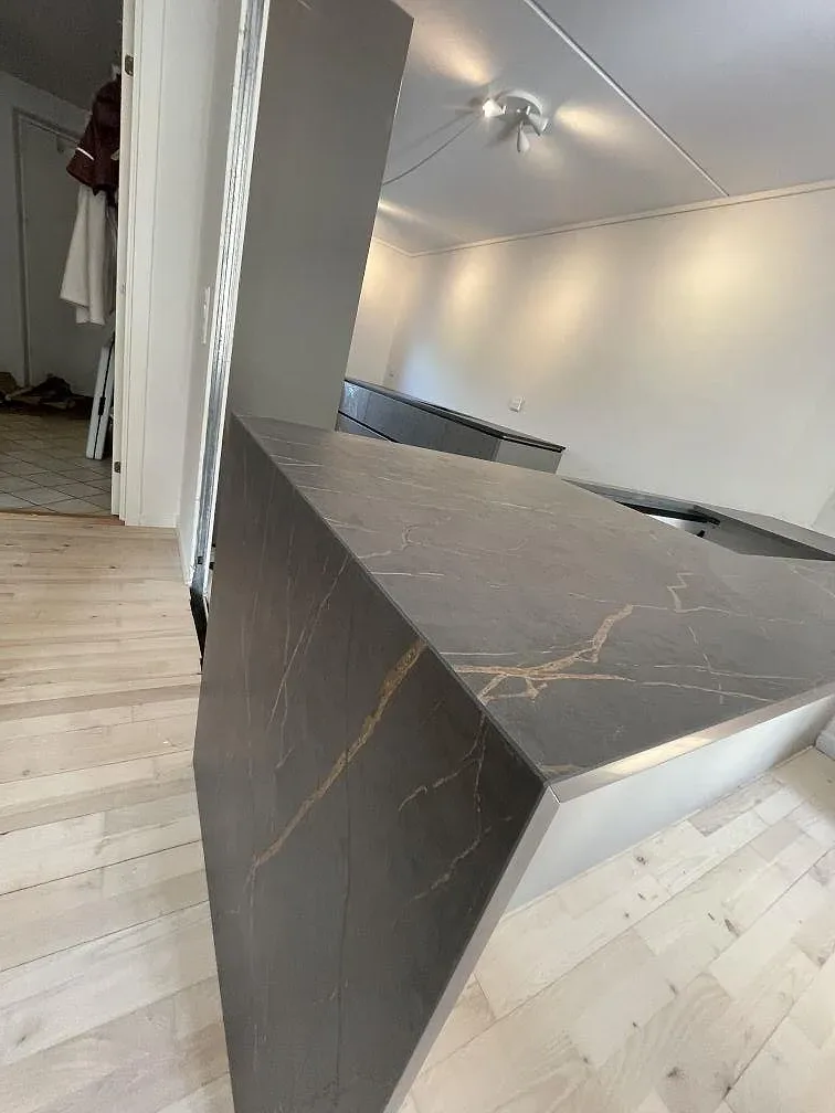 Närbild på vattenfallskanten i Dekton Laurent där den matta mörka keramiken visar varma guldådror, kök i Allerød.