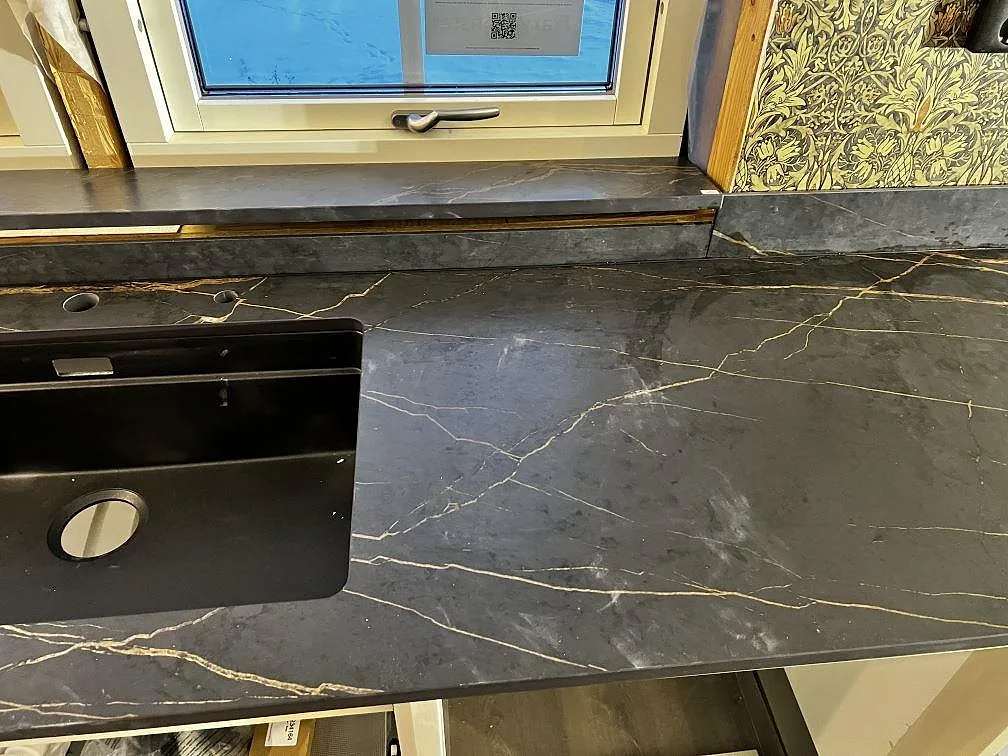 Sinkdetalj i matt Dekton Laurent med svart underlimmad diskho, fönsterbänk och bänkskiva med guldådring i Gränna.